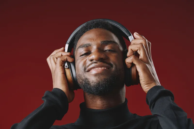 Smiling young African American man wearing headphones, enjoying music against a vibrant red background, conveying a sense of happiness and relaxation