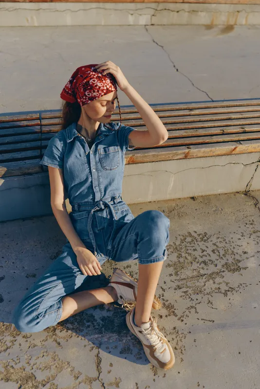 Lifestyle woman in modern boho-western denim street style with a red bandana, casual posture, and film color tones in outdoor urban setting.