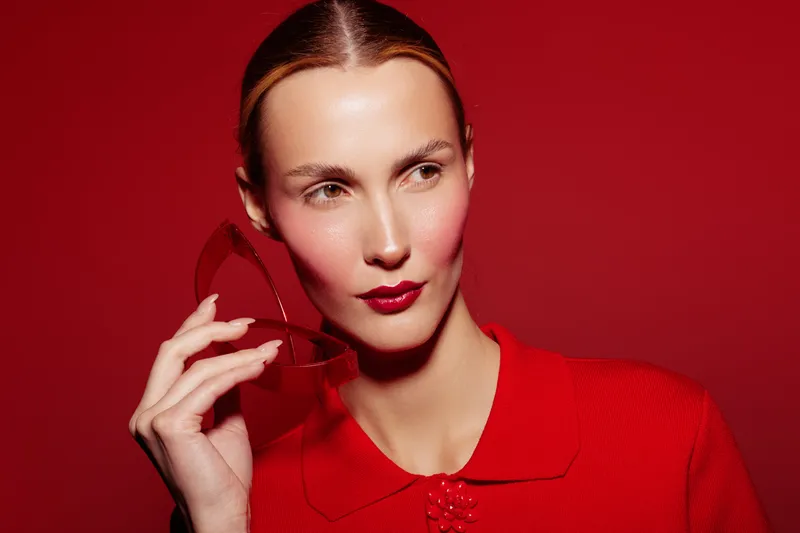 Portrait of a stylish woman in red holding a red cocktail glass against a red background. Concept of fashion, elegance, and modern lifestyle with vibrant color contrast.