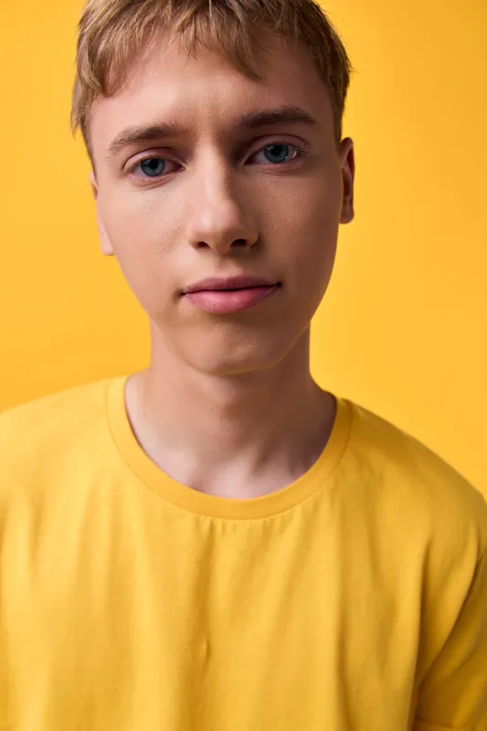 Bright close up of a youthful male model wearing a yellow shirt against a warm yellow backdrop, tight lens, clean lighting, casual fashion and studio shot style for lifestyle use
