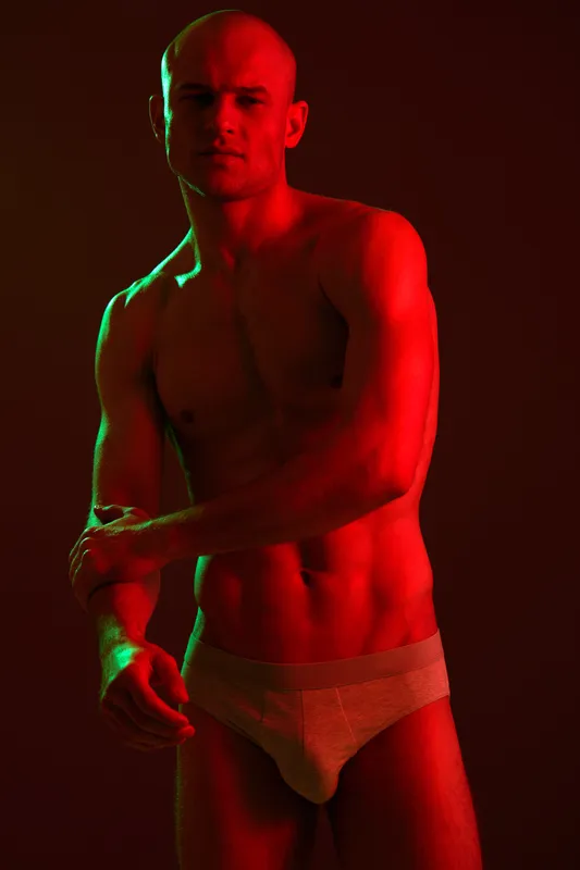 Athletic man posing in dramatic lighting, showcasing his physique with a confident expression. The bold colors create a striking visual impact and enhance the atmosphere.