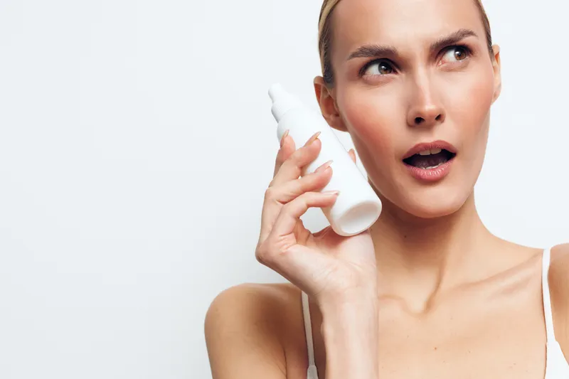Woman applying face cream with white applicator, closeup on light clean background. Skincare beauty routine, hygiene and wellness concept. Soft very calm studio lighting.