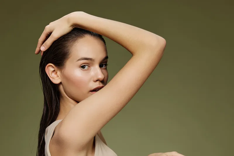 Elegant young woman with natural beauty poses gracefully against a soft green background, showcasing healthy skin and hair in a minimalistic style