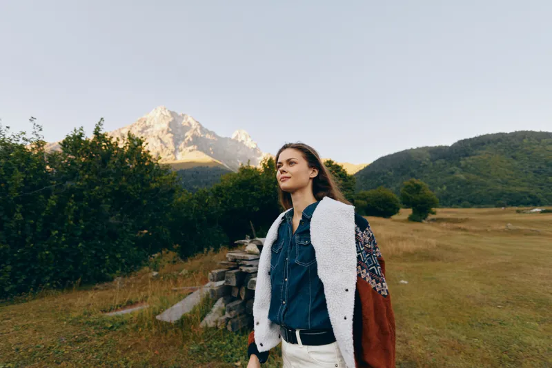Woman mountain nature travel meadow hiking portrait outdoor scene of a young woman walking through alpine grass and wildflowers, casual clothing and scarf, enjoying scenic view and peaceful adventure.
