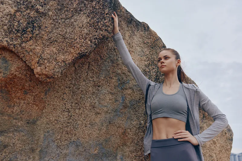 Athletic young woman in stylish workout clothes poses confidently against a natural rock background, showcasing her strength and determination in a fitness lifestyle setting