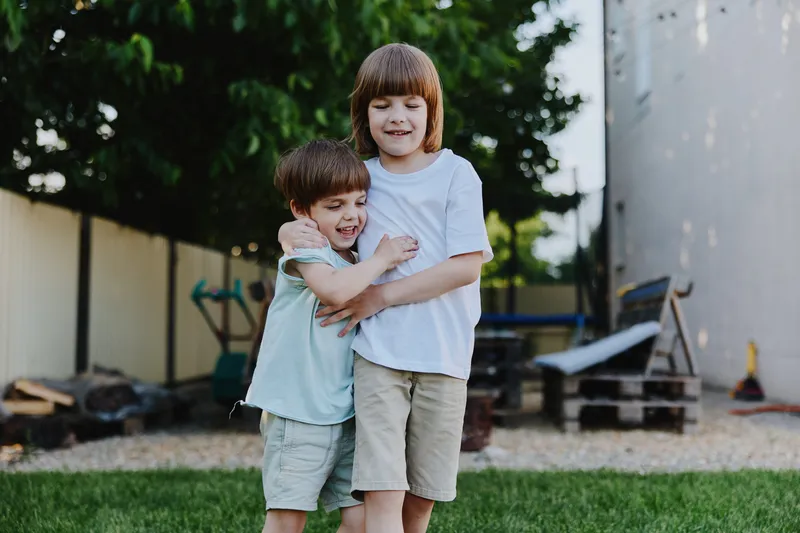 Happy children enjoying their playful moment outdoors, embracing each other in a sunny backyard filled with greenery and playful elements.