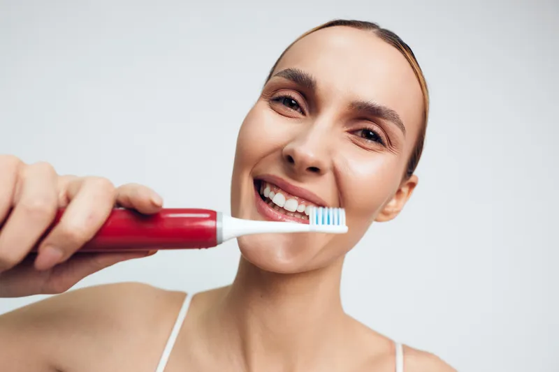Woman brushing teeth with a toothbrush, oral hygiene routine, smiling, clean toothpaste foam near lips, close up portrait against bright bathroom background, personal care concept daily
