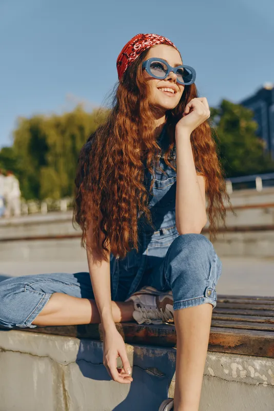 lifestyle woman in modern boho-western denim street style wearing sunglasses and a red bandana with long curly hair and film color tones