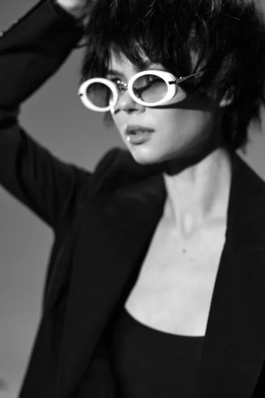 Black and white portrait of a stylish woman wearing white sunglasses and a dark blazer with a soft focus background.