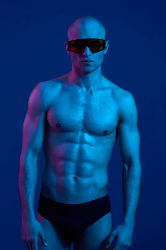 Athletic man showcasing his fitness physique in striking blue lighting. The muscular features and confident stance create an impactful black and white visual experience.