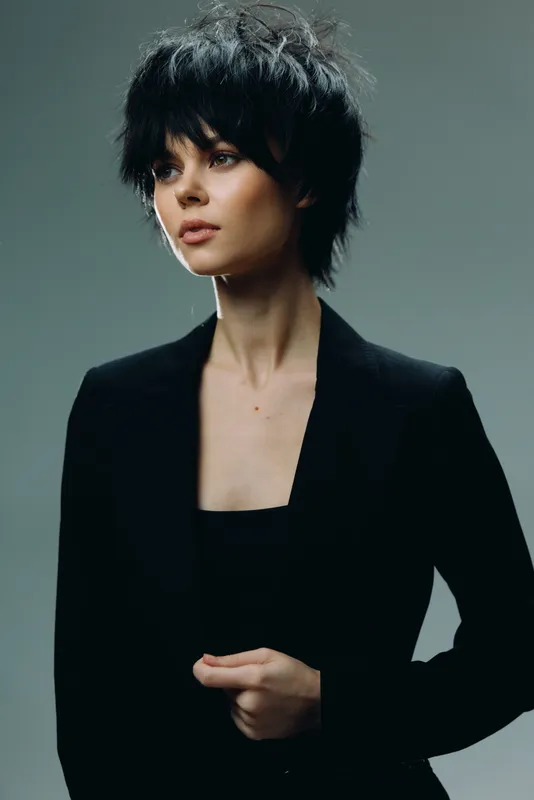 Woman in black blazer with short hair posing, elegant style, neutral background, thoughtful expression, fashion portrait
