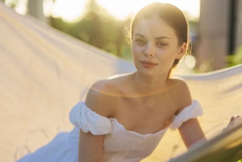 Young woman in a white dress enjoying a sunny day, lying in a hammock, with soft light creating a dreamy atmosphere, perfect for relaxation and tranquility