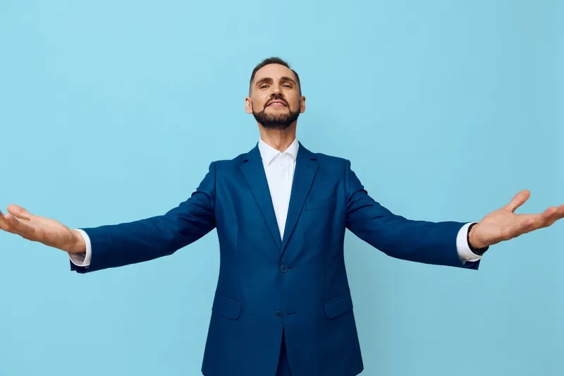 A professional businessman stands with arms open against an isolated colored backdrop, projecting confidence and power. The scene emphasizes leadership, success, and positive emotion in a modern
