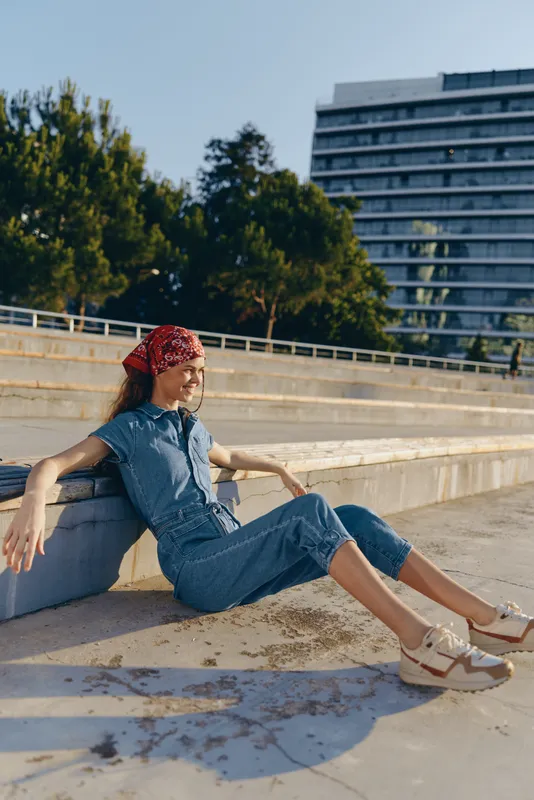lifestyle woman in modern boho-western denim street style sitting relaxed outdoors with film color effect under bright sunlight in urban setting