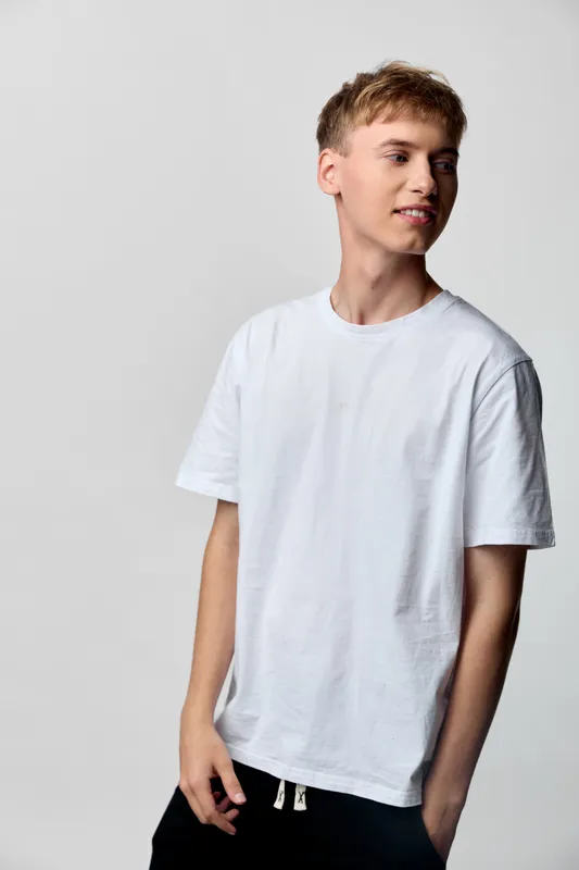 Man in a white t shirt stands in a neutral studio, casual clothing and relaxed pose convey youthful fashion, simple wardrobe and clean aesthetic, smiling expression in a minimal, contemporary look