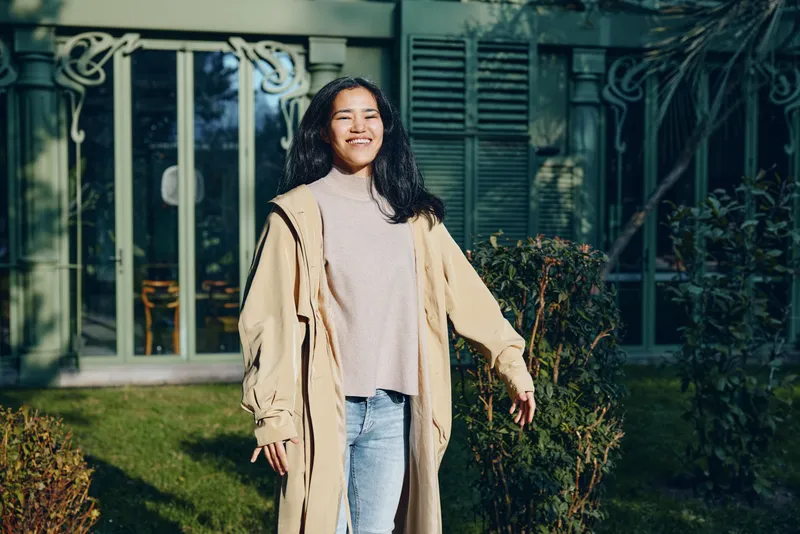 Coat, casual, outdoor fashion with a smiling woman in a beige overcoat standing in a sunlit garden.
