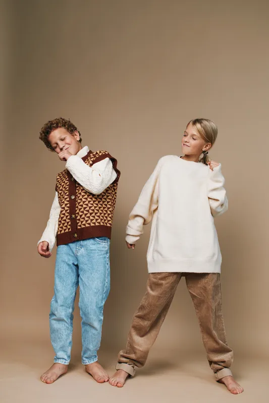 Authentic depiction of two children at play, showcasing school lifestyle through casual outfits, candid pose, and gentle movement in a warm studio setting.