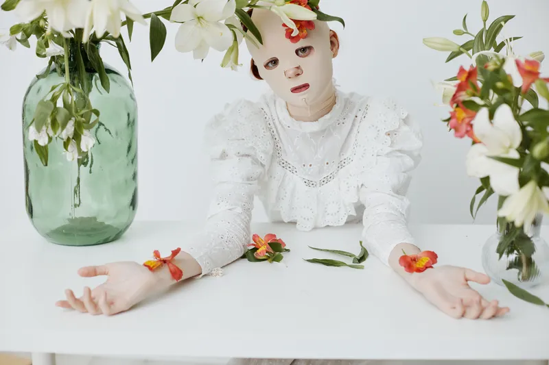 A serene model in white attire with floral accents, surrounded by vases of vibrant lilies, conveying tranquility and elegance, perfect for wellness themes