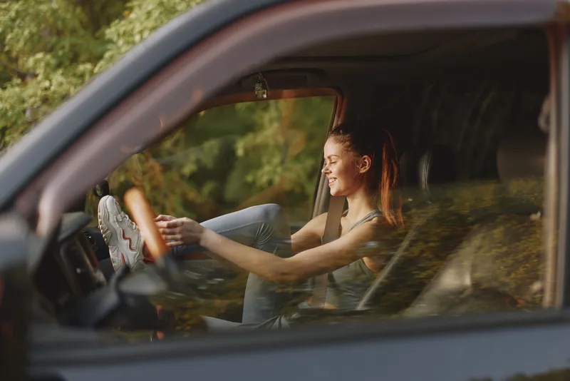 Young woman enjoying a sunny day driving a car, smiling with bare feet on the dashboard, representing freedom and joy of travel