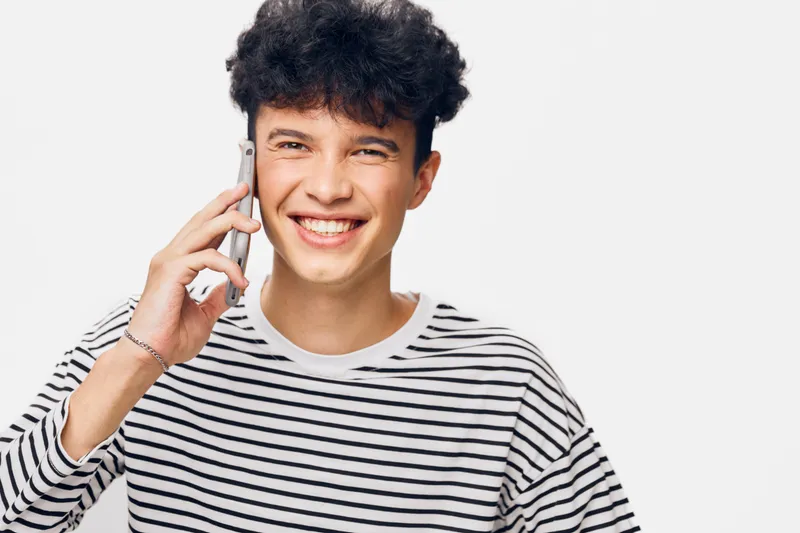 smiling man talking on phone wearing striped shirt, young adult with curly hair, bright studio background, casual lifestyle expression
