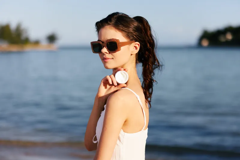 Woman wearing sunglasses by the sea, enjoying sunny weather with calm water and clear blue sky, summer lifestyle and relaxation concept.