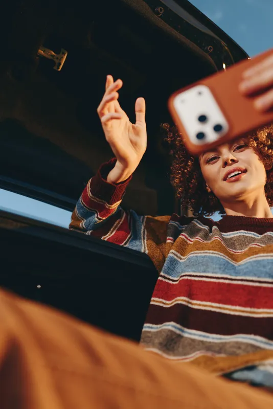 Woman lifestyle by car window, wearing striped sweater, making peace hand gesture, smiling in natural light, casual travel mood, soft cinematic focus