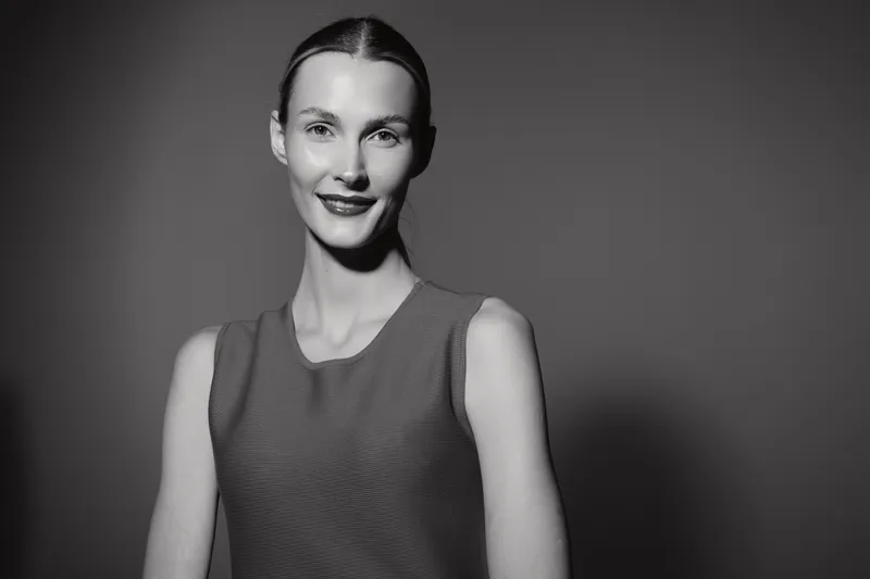 Portrait of a smiling Caucasian woman with fair skin wearing a sleeveless top on a dark background. Concept of confidence and natural beauty.