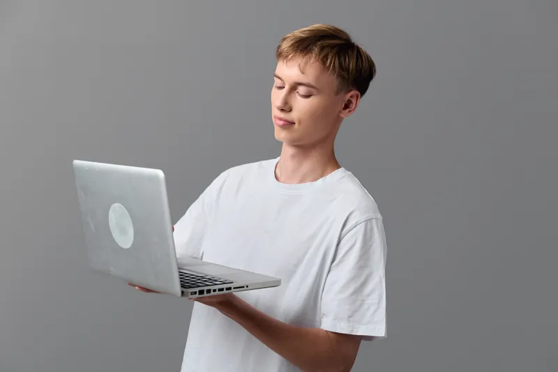 Laptop held by a casual young man in a white shirt, showcasing technology usage, handheld device, computing in a modern studio with focused expression and minimal backdrop
