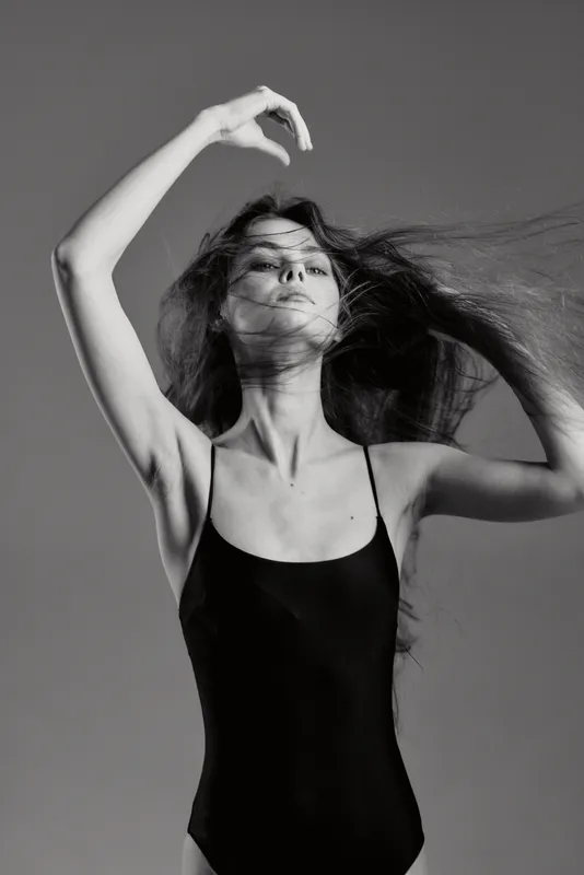 Black and white portrait of a graceful woman in a black bodysuit with flowing hair and expressive pose, evoking elegance and movement