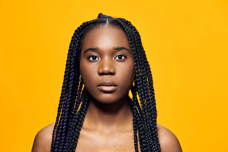 Portrait of a young woman with braided hair against a bright yellow background, exuding confidence and strength, perfect for empowerment themes