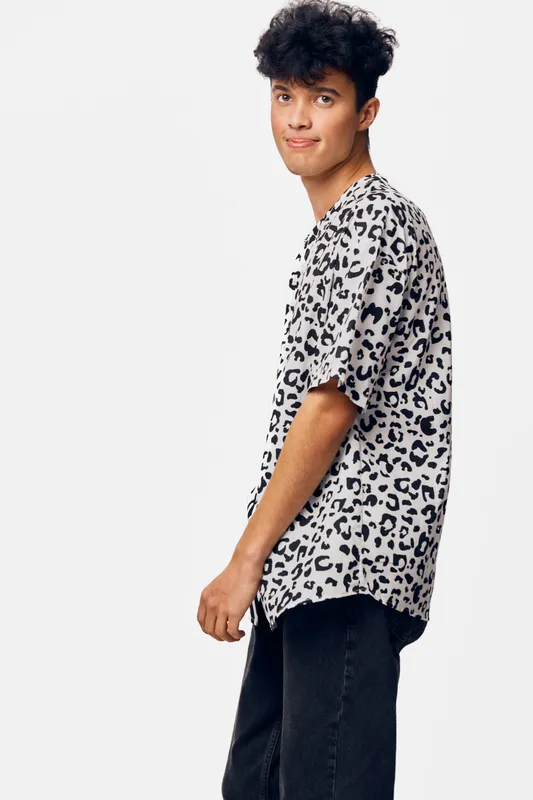 young man wearing leopard print shirt stands casually against white background, with relaxed expression and modern hairstyle, showcasing casual fashion style.
