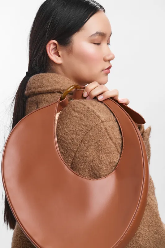 asian woman wearing a cozy coat and carrying a round leather bag, profile view, calm expression, minimal backdrop, fashion focused, soft light, contemporary style, poised urban look.