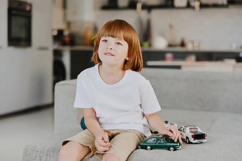 Adorable boy playing with toy cars in a cozy living room. Bright, cheerful atmosphere and playful expression capture the joy of childhood moments.