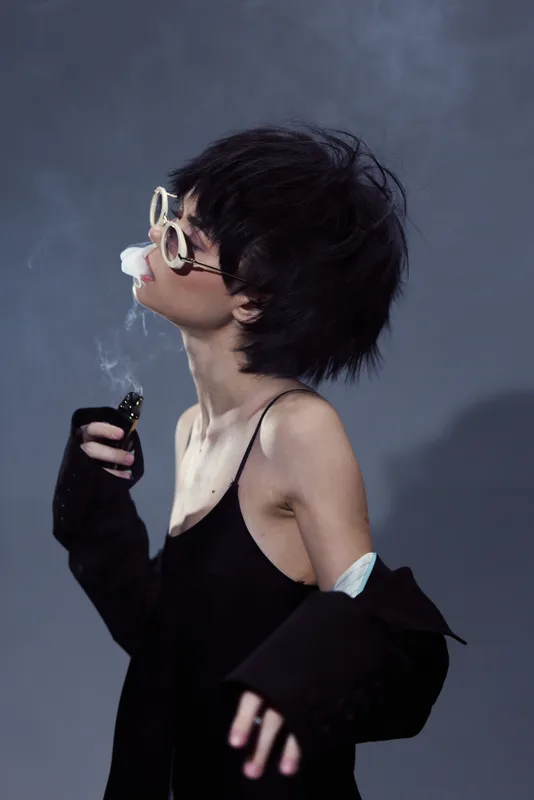 Young woman smoking stylishly with sunglasses in moody setting, casual fashion, contemplative mood, dark background.