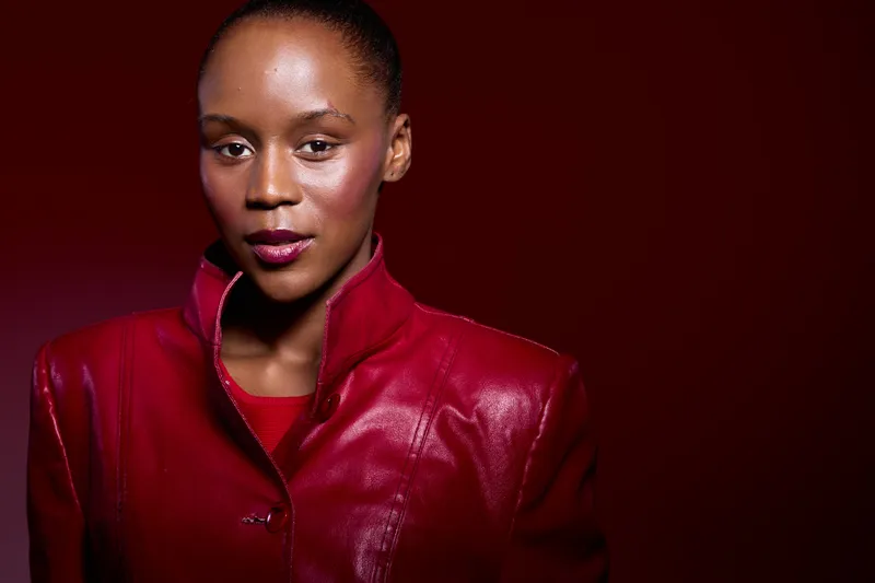 Portrait of confident African woman with dark skin wearing red leather jacket on red background. Studio lighting highlights natural beauty and fashion style with serious expression.
