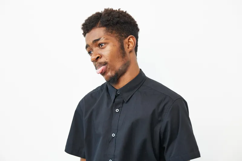 Black man with a stylish haircut, wearing a black shirt and showing a thoughtful expression. Capturing a moment of reflection and individuality.