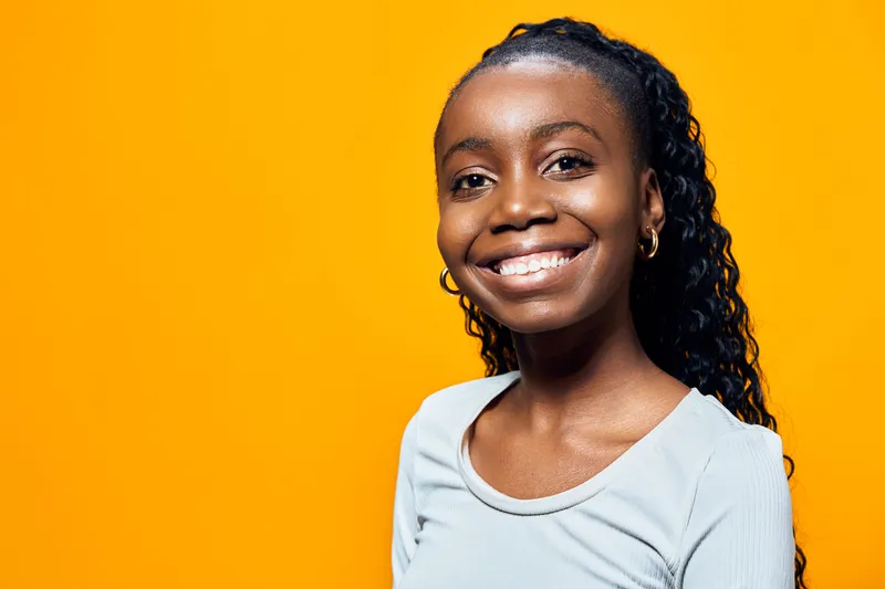 Young black woman smiling brightly against a vibrant yellow background, showcasing joy and confidence in casual attire Ideal for diversity and positivity themes