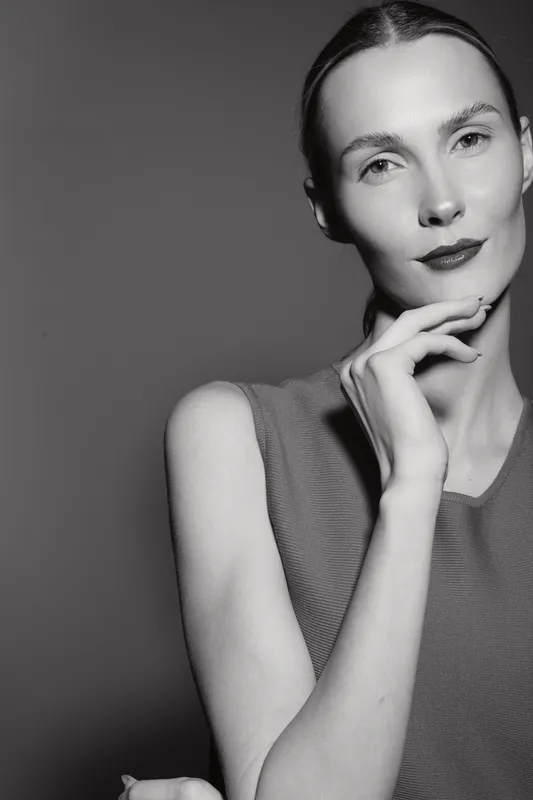 Elegant white woman with fair skin poses confidently with hand near face in black and white studio portrait. Concept of beauty, fashion, and minimalistic style with natural light.