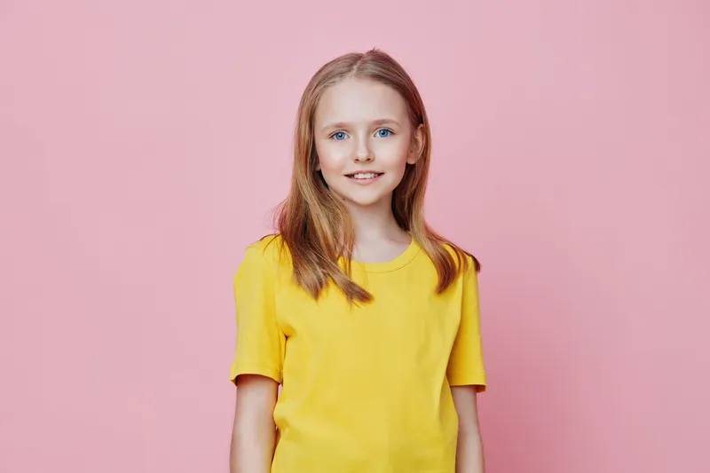 Cheerful young girl in a bright yellow shirt against a pink background, expressing joy and confidence, perfect for themes of happiness and childhood