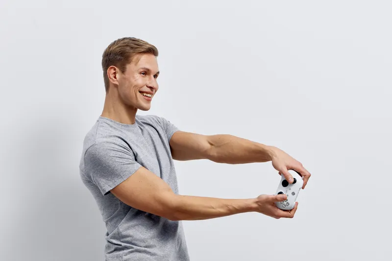 smiling young caucasian man in grey t-shirt holding game controller playing video games with joy isolated on plain white background digital entertainment concept
