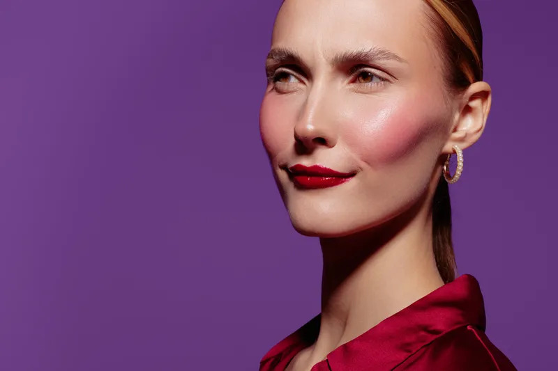 Close-up portrait of confident woman with red lipstick and earrings on purple background. Concept of beauty, fashion, makeup, and elegance with studio lighting and smooth skin texture.