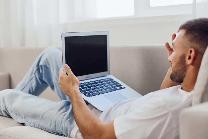 Relaxed man working on a laptop at home, showcasing a cozy and modern lifestyle. Perfect for themes of remote work and digital nomadism in 2025.