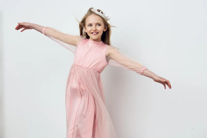 Cheerful girl in a flowing pink dress twirling gracefully against a light background, showcasing joy and playfulness in a whimsical fashion