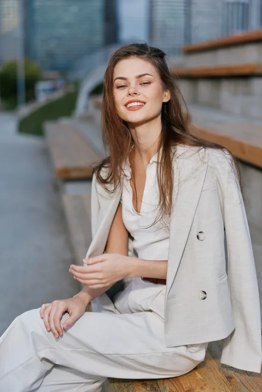 young woman in light business casual outfit sitting outdoors smiling serene confident urban background autumn fashion BUSINESS