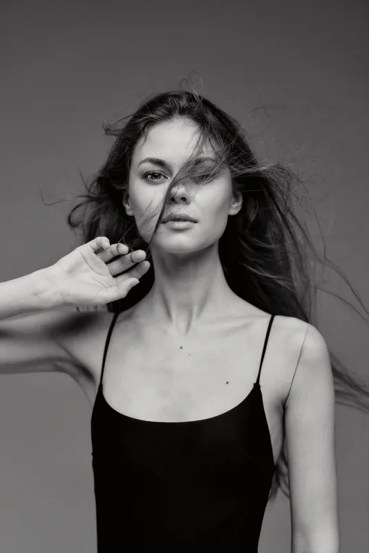 Black and white portrait of a young woman with loose hair wearing a black dress, conveying natural beauty and elegance.
