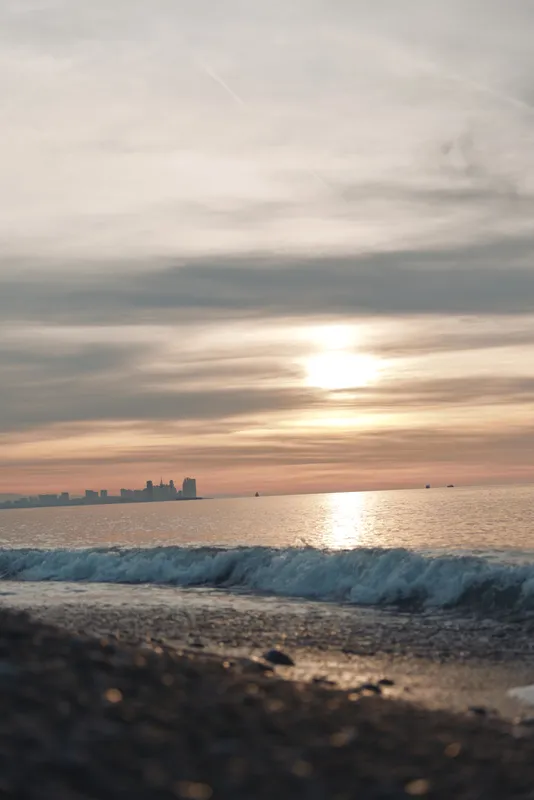 sunset beach, ocean waves, calm horizon, soft light, pebbles on sand, quiet water and sky glow, serene coastal scenery for a peaceful end of day at sea