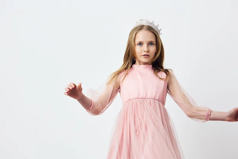 Young girl in a pink dress with tulle sleeves, showcasing a surprised expression against a minimalist background, perfect for children s fashion and emotional portraits