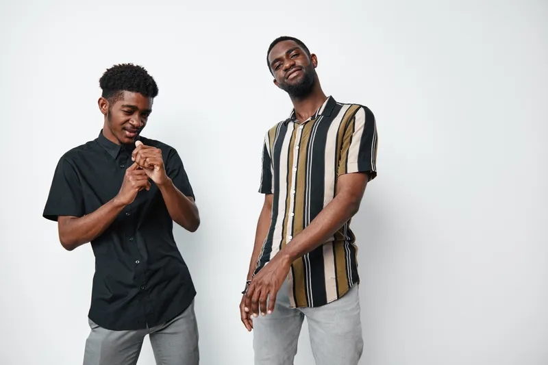 Two young black men with dark skin standing and posing in casual clothes against white background. African ethnicity, smiling and relaxed in studio portrait.