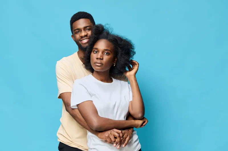 Young African couple embracing and smiling together against a vibrant blue background, showcasing love, connection, and modern casual fashion