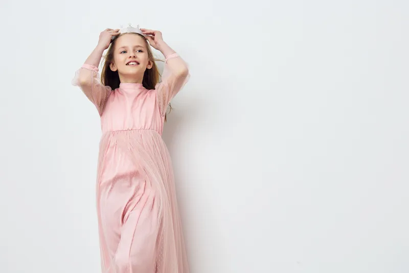 Joyful girl in a pink dress expressing happiness, posing against a minimalistic light background with soft pastel tones, ideal for childhood and celebration themes